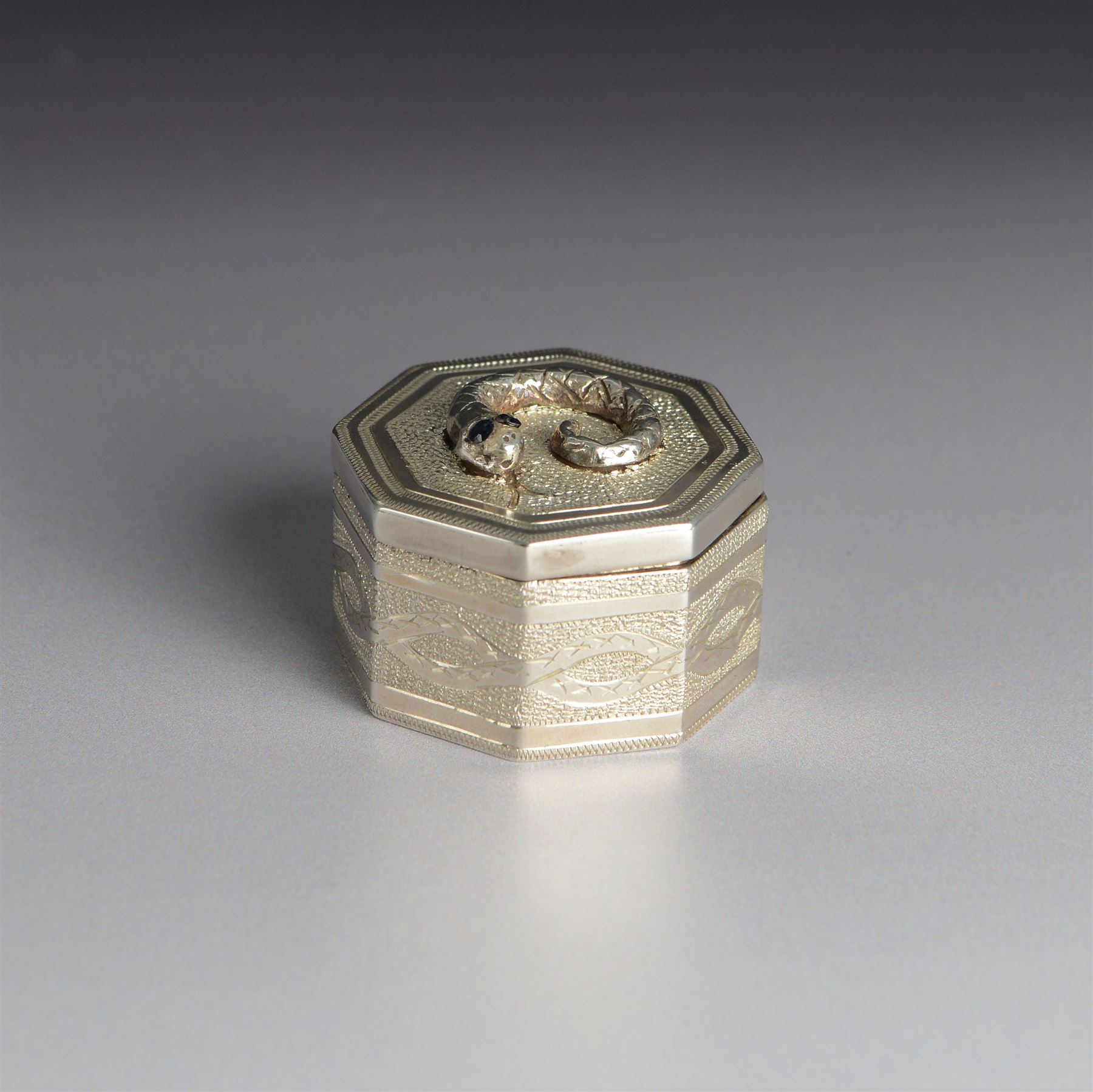 Silver trinket box, of hexagonal form, engraved with entwined snakes to body and decorated to the removable cover with a snake with sapphire set eyes, hallmarked Jonathan Braganza, London 2012, H3cm, W4cm