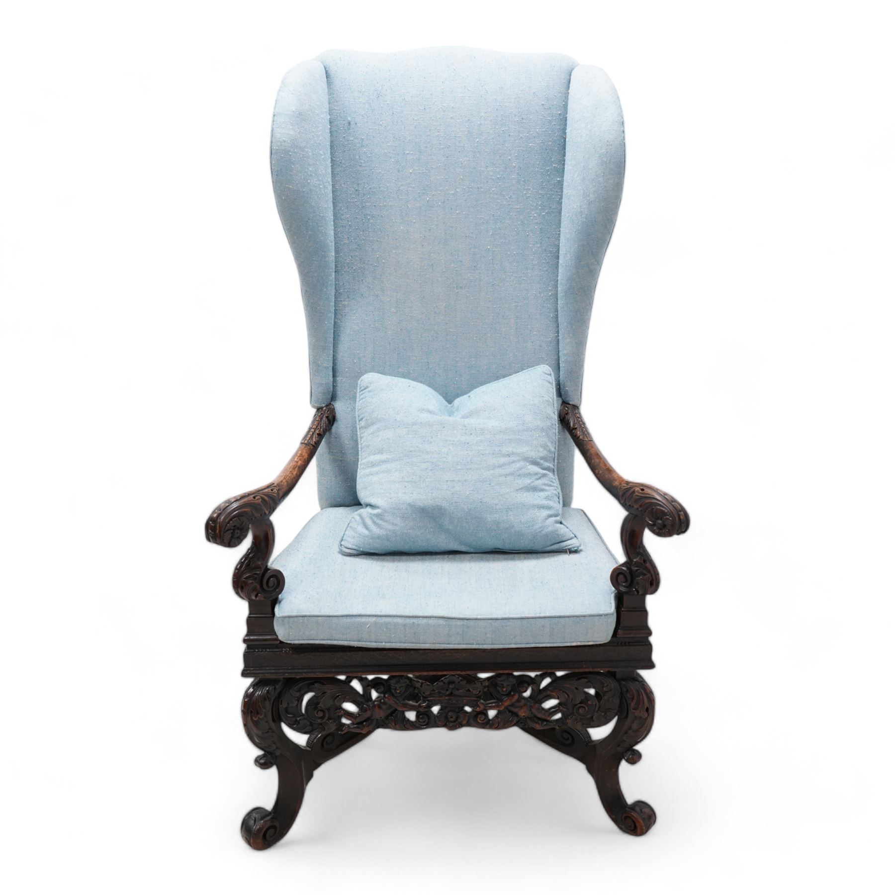 Carolean design walnut and oak wingback open armchair, the high wingback upholstered in light blue herringbone fabric, acanthus leaf carved arms with scrolled terminals and on scrolled supports, cane work seat with squab cushion and scatter cushion, the lower rail carved and pierced with putti holding crown surrounded by curled acanthus leaves, leaf carved S-scroll supports united by Scrolled X-framed stretchers 