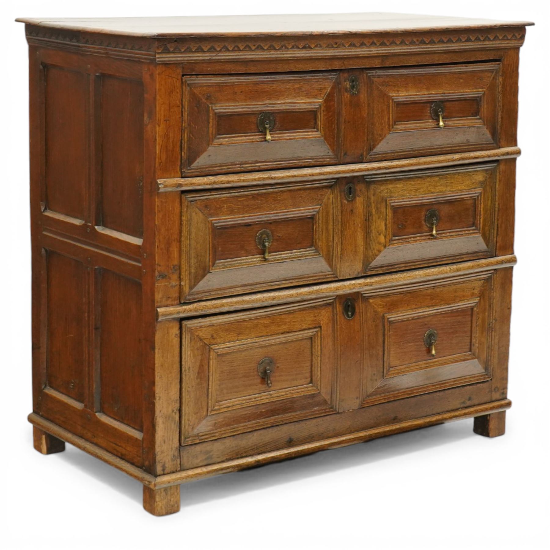 18th century oak chest of drawers, rectangular plank top with chip carved frieze, fitted with three long geometrically panelled drawers with applied mouldings, later brass drop handles, on stile supports, panelled sides and boarded back
