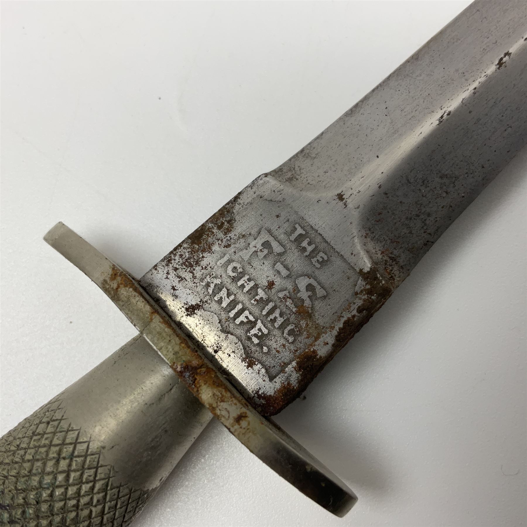 First Pattern Fairburn Sykes ''F-S'' Fighting Knife by Wilkinson Sword Ltd., the 17cm double edge steel blade with raised medial ridge to each side, each side of the ricasso with a recessed panel, one side with maker's name, the opposing side etched THE F~S FIGHTING KNIFE, with nickel plated brass recurving crossguard and diamond cut grip; in leather scabbard with metal chape