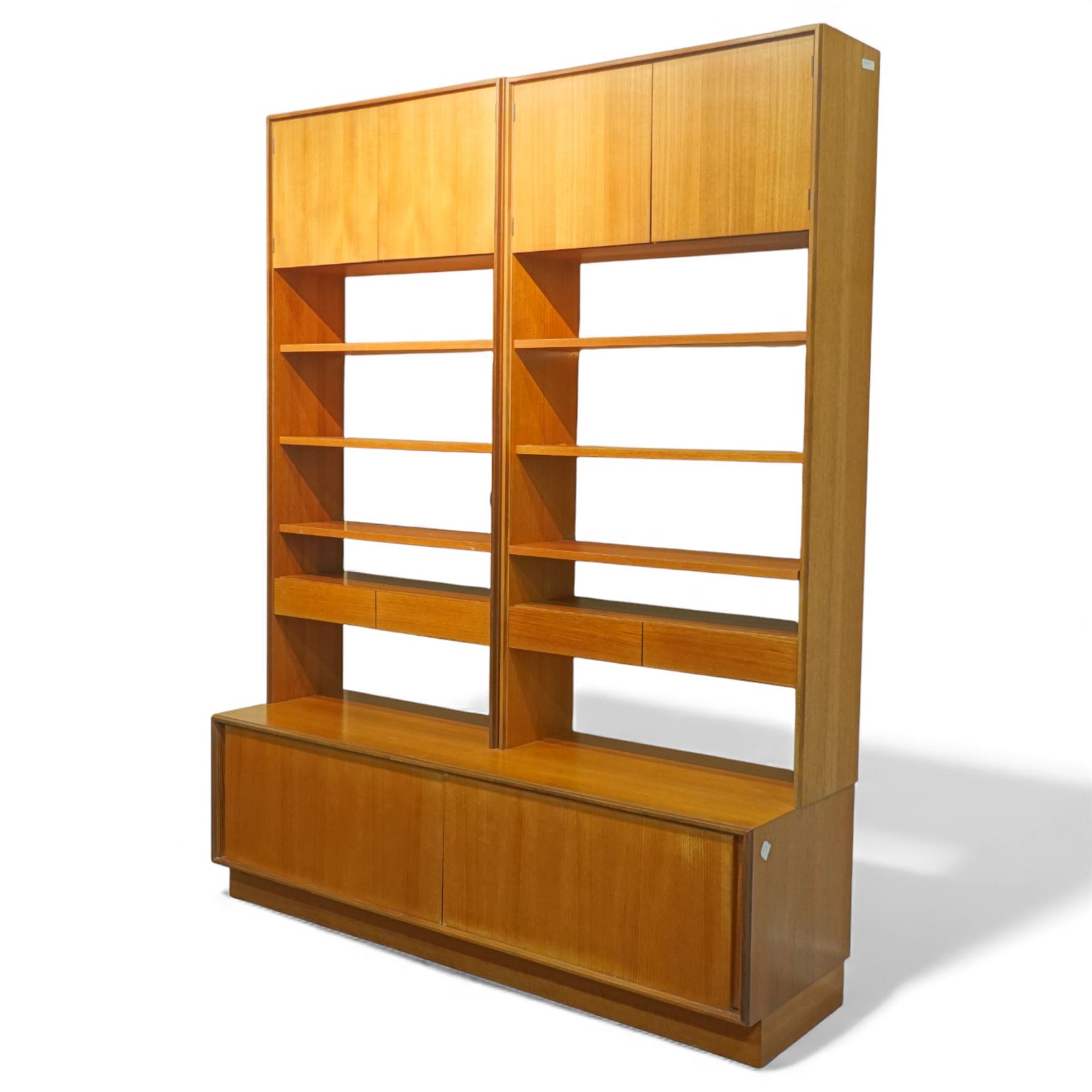 G Plan - 'Form 5' teak modular bookcase unit, comprising two upright sections with upper cupboard compartments enclosed by hinged doors, open adjustable shelving below, fitted with a pair of central drawers to each section, raised over a long base cabinet with sliding cupboard doors