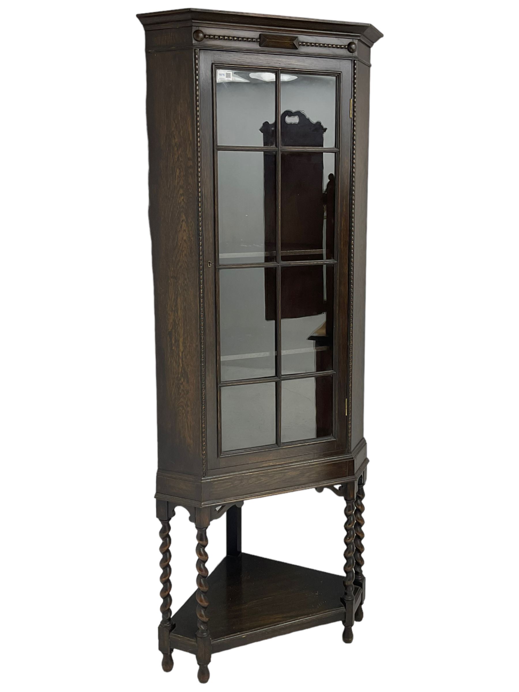 Early 20th century oak corner display cabinet, enclosed by glazed door, on spiral turned supports joined by undertier 