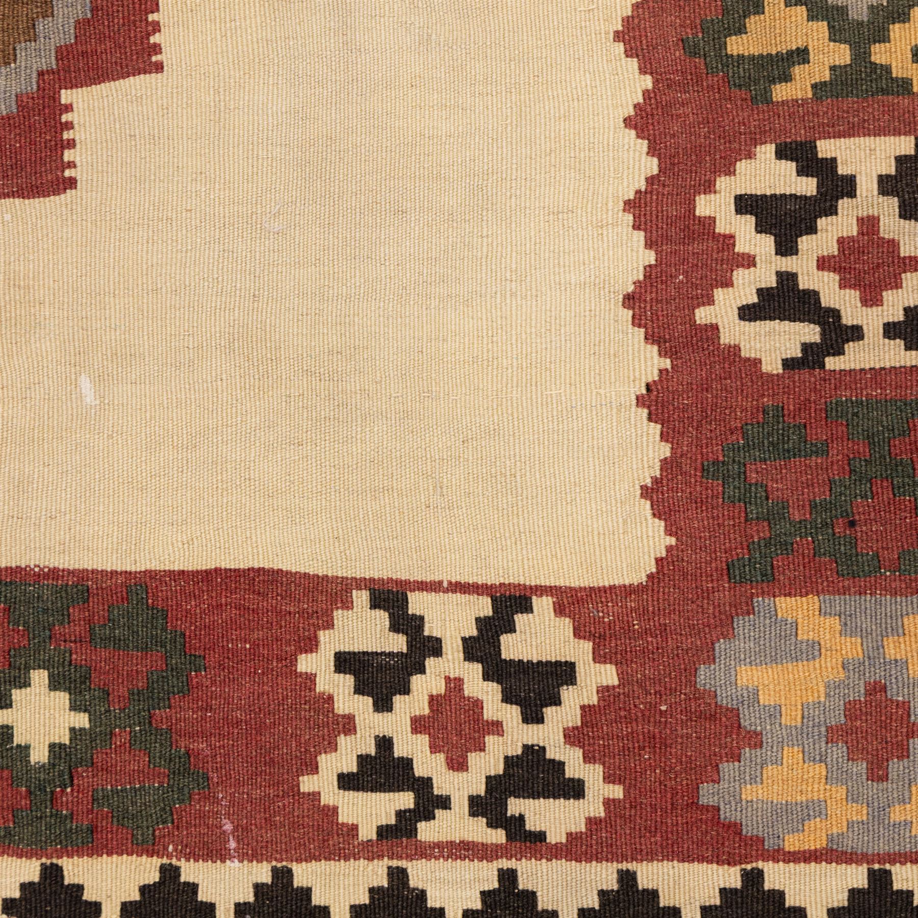 South West Persian Qashqai kilim, woven in flatweave in earthy tones, camel brown, ivory, olive, green, black, and madder red with three bold lozenge-shaped medallions, geometric borders incorporating stepped, hooked, and rosette motifs 