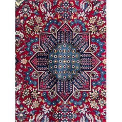 Central Persian Isfahan Carpet, hand-knotted, featuring a bold central rosette medallion on a rich red field, flanked by stylised floral sprays, scrolling foliage and mythical animals, within a broad indigo border decorated with alternating cartouches and flowerheads