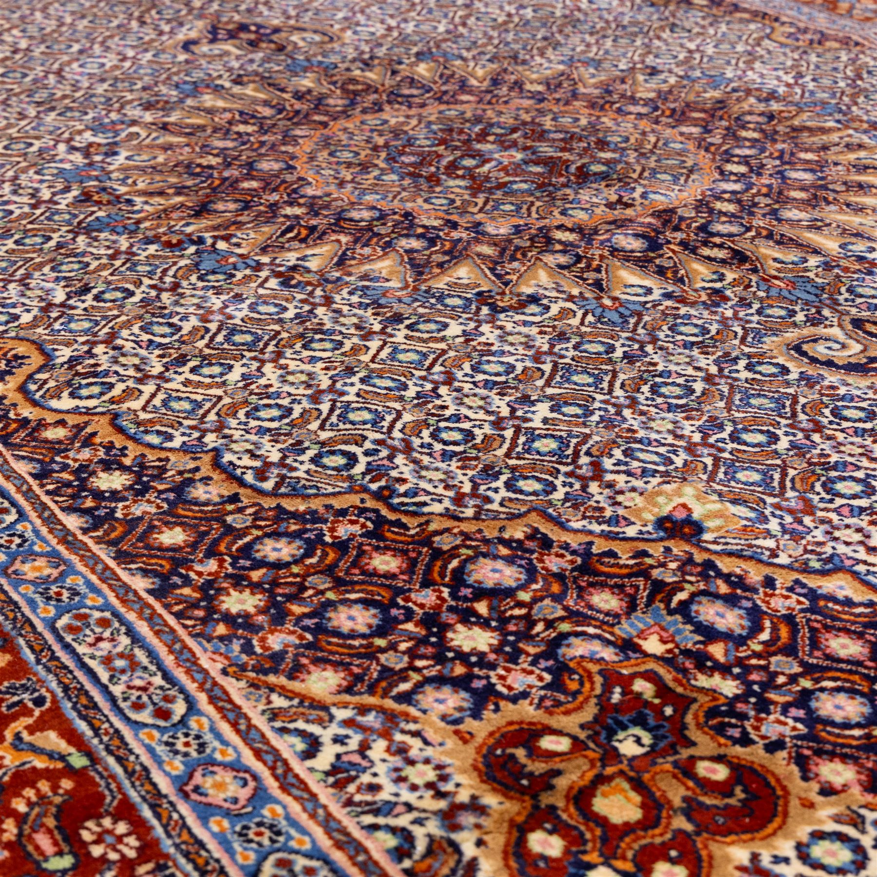 North Eastern Persian Moud hand-knotted carpet, field with central lobbed medallion with radiating serrated palmettes and spandrels in a densely worked all-over ground of small floral rosettes and geometric blossoms within a wide floral border flanked by multiple guard borders in a palette of indigo blue, ivory, terracotta, turquoise, and muted gold, with cotton fringe ends 