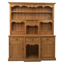 20th century country style waxed pine housekeeper’s cupboard, upper section with moulded cornice, shaped aprons and open shelving around central drawer arrangement, the lower section fitted with three drawers and two cupboards with panelled doors, raised on a plinth base