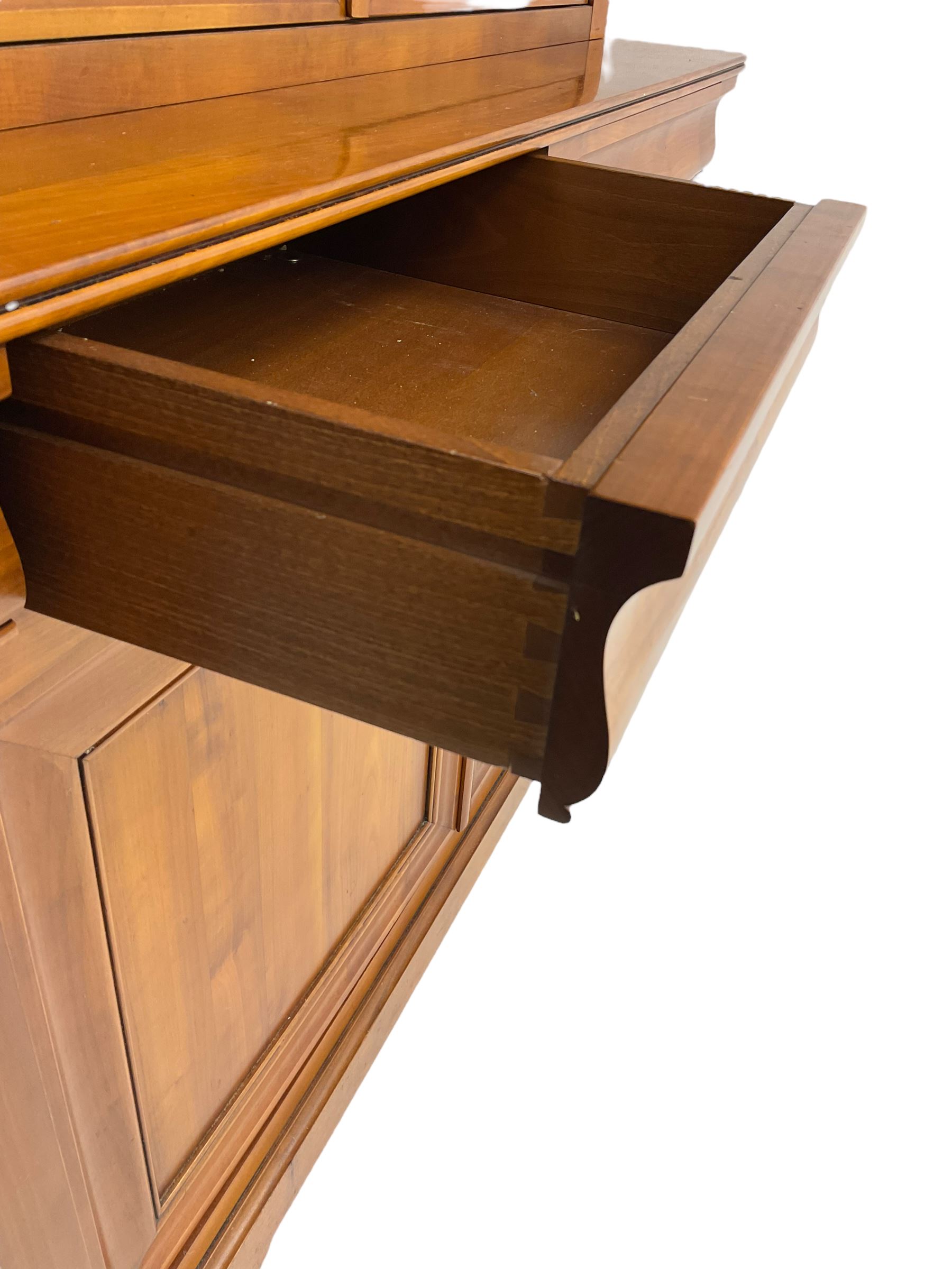 French cherry wood bookcase on cupboard, projecting cornice over two cupboard doors with bevelled glass panels enclosing three adjustable shelves, base fitted with two cushion drawers over double cupboard