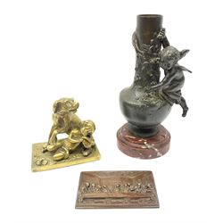 A bronzed spelter vase detailed with a fruiting vine and mounted with a cherub, raised upon a circular stepped red marble effect base, overall H24cm, a brass figure modelled as a dog and child, H11.5cm, and a base metal plaque illustrating the last supper in relief, H7.5cm L12cm. (3). 