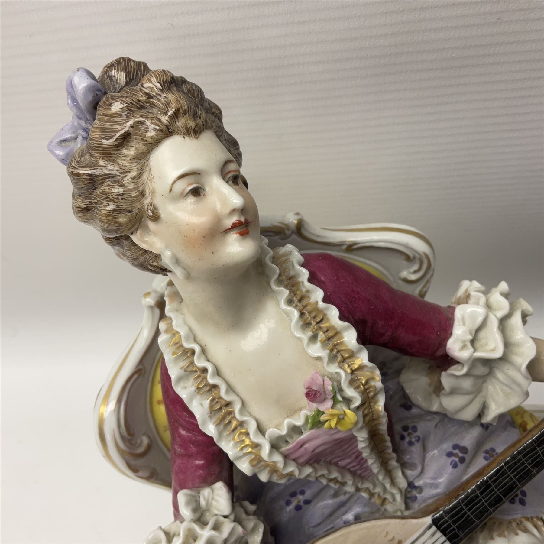 20th century Naples figure group, modelled as a seated female figure playing the lute seated, before a male figure stood holding a sheet of music, each in period dress, upon an oval base with gilt heightened scroll edge, with crowned N mark beneath, H31.5cm L33cm
