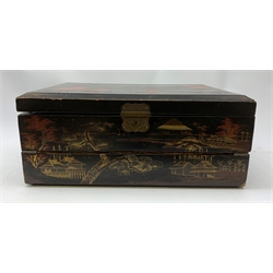  A 20th century Chinese black lacquer and gilt detailed writing box, decorated with figures, pagodas and cranes amidst a mountainous landscape, the hinged cover opening to reveal a compartmented interior and fold out baize lined slope, H20cm L46.5cm D31.5cm.   