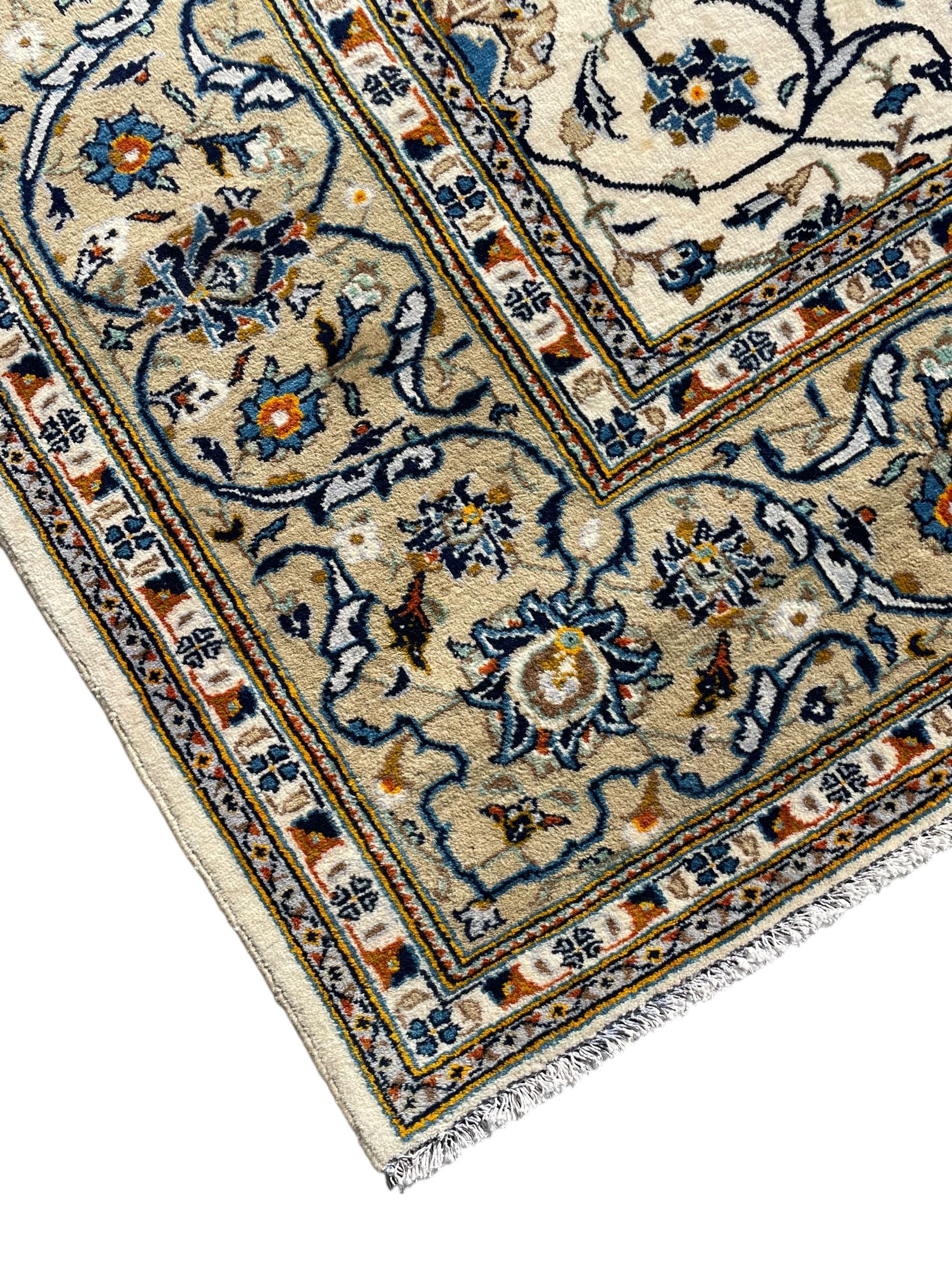 Persian Kashan ivory ground carpet, overall floral design, the field decorated with scrolling and interlaced leafy branches interspersed with palmettes, scrolling border decorated with stylised plant motifs, within floral pattern guard stripes 