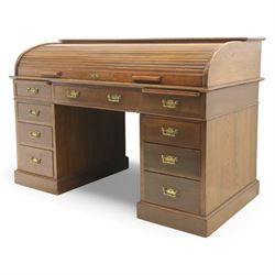 Edwardian oak roll-top desk, the tambour enclosing a fitted interior of pigeonholes and dividers, over a central kneehole flanked by twin banks of drawers with brass handles, on plinth bases