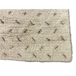 Cream ground woollen rug, thick shaggy pile, central shaped medallion with curled stylised foliate decoration 