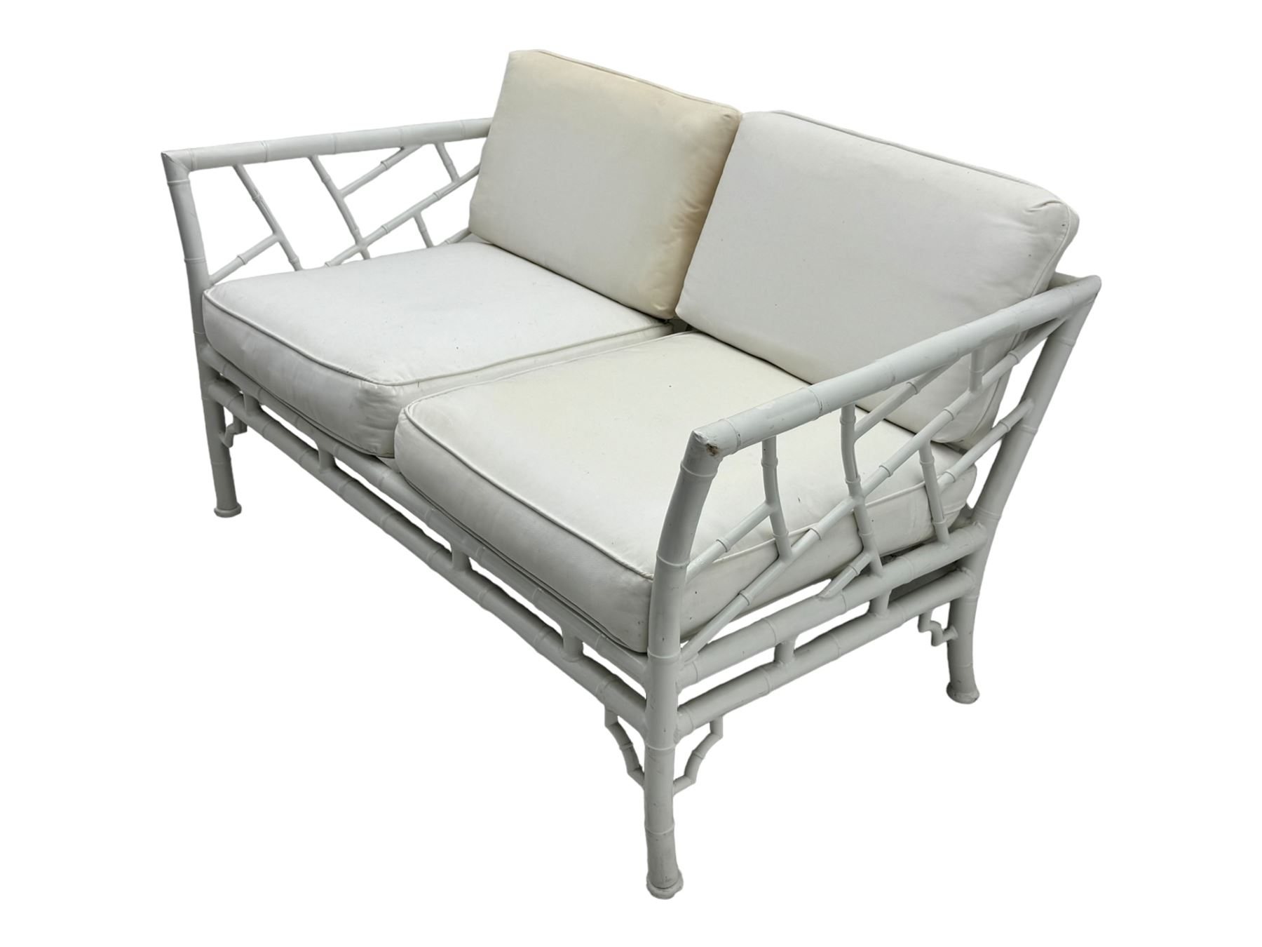 Late 20th century faux bamboo conservatory sofa, white painted frame with geometric openwork back and sides, loose cream cushions, on cylindrical supports (W134cm, D76cm, H80cm); matching armchair (W75cm, D76cm, H80cm); matching coffee table with glass insert (W46cm, D45cm, H36cm)