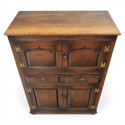  Late 20th century oak four door cupboard in the manner of Titchmarsh and Goodwin, rectangular plank top above two pairs of fielded panel doors with shaped raised panels, central arrangement of a brushing slide above two short drawers with brass swan neck handles and pierced backplates, enclosed by further pair of panelled cupboard doors, fitted with brass butt hinges and turned wooden knobs, raised on plinth base