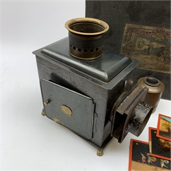 Ernst Plank magic lantern with black japanned body, brass chimney and lion paw feet, in original ebonised box with seven 24cm coloured glass slides including Transport Through the Ages etc, the hinged lid with paper labels to both sides W36cm