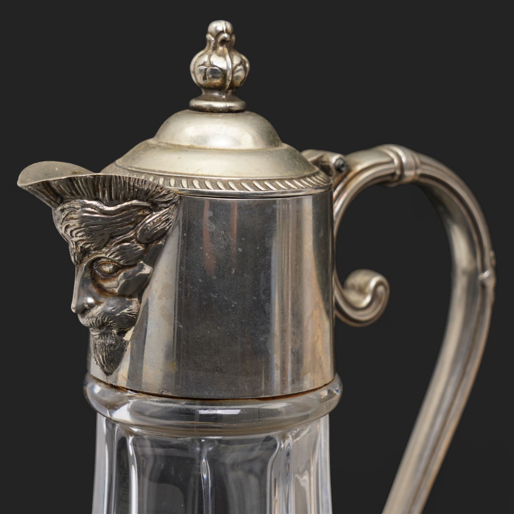 Composite plaque, depicting Sprites in a garden, with inset 'Arts and Commerce Promoted' medallion to reverse, 20cm x 33cm; together with a moulded glass Claret jug with silver plated mount H30cm 