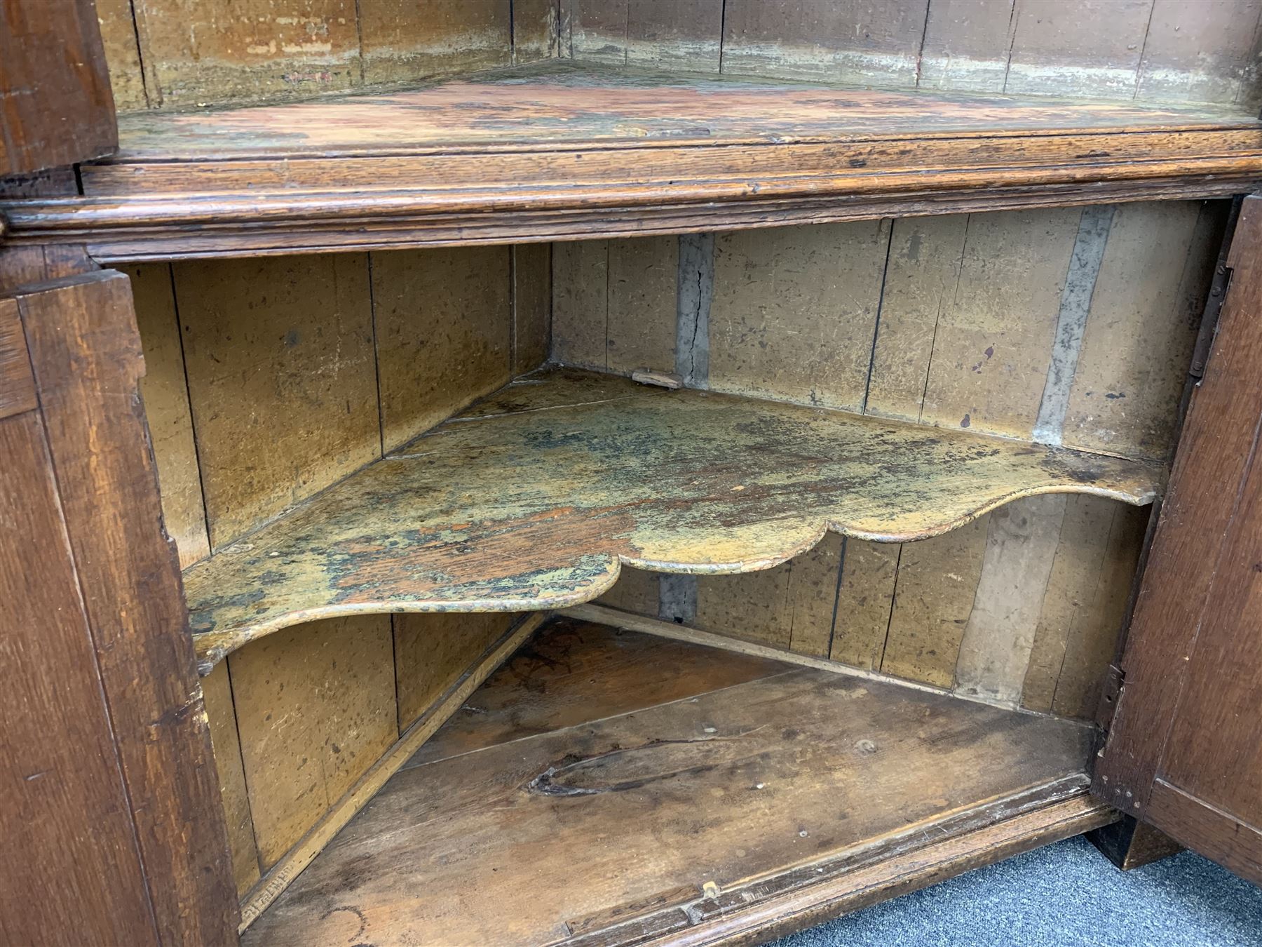 Large George III oak corner cupboard, projecting cornice over two stepped arch doors with fielded panels and blind fret work spandrels, flanked by fluted uprights, cupboard below enclosed by two fielded panel doors, the painted interior fitted with shaped shelves
 