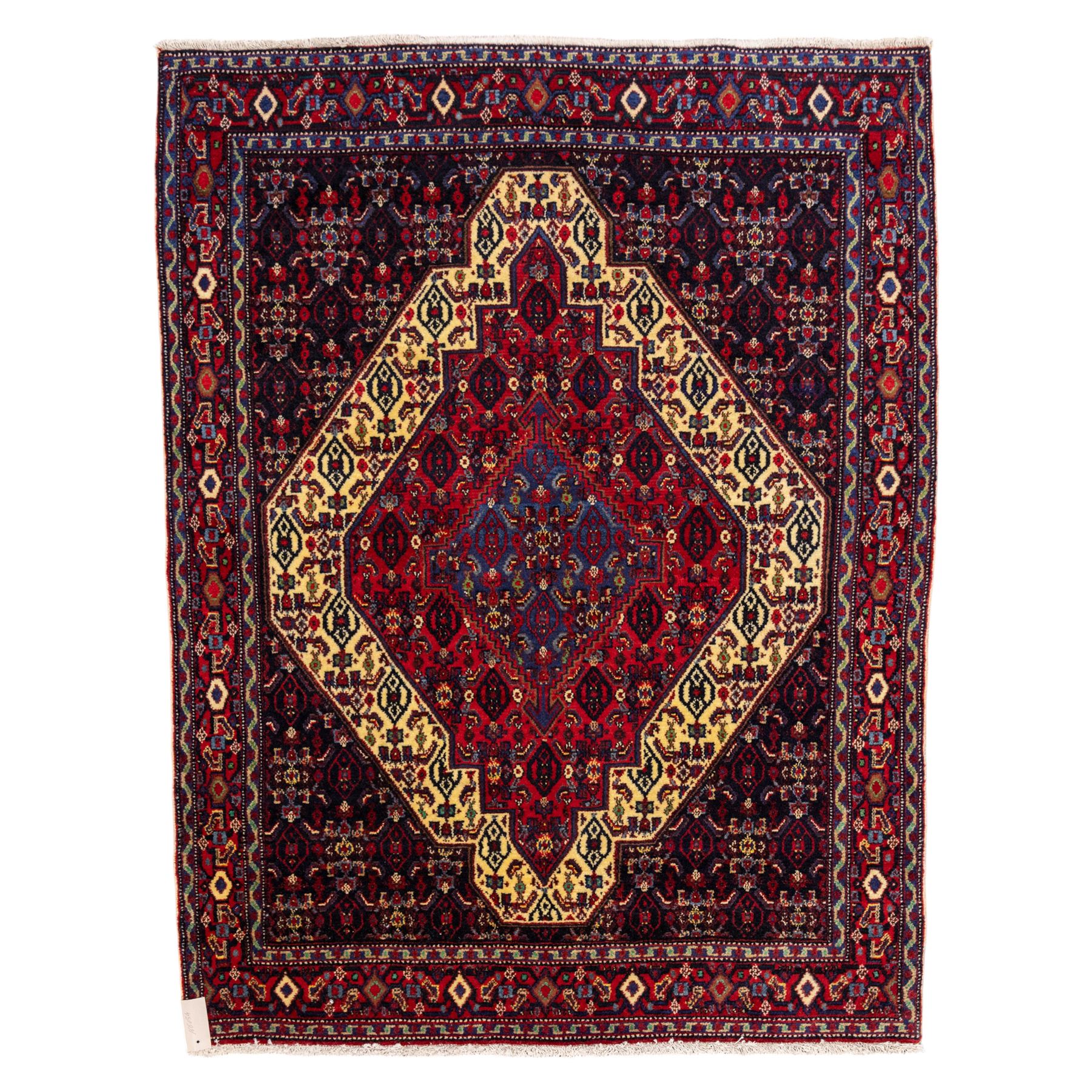 North West Persian Senneh hand-knotted rug, dark indigo field with a central bold stepped lozenge medallion of madder red and deep blue, enclosed within an ivory serrated contour forming a cruciform outline, medallion with repeating boteh and floral devices, field decorated with an all-over Herati pattern of rosettes enclosed by angular leaves principal border of madder red ground decorated with alternating floral heads, flanked by narrow guard stripes, with cotton fringe ends 