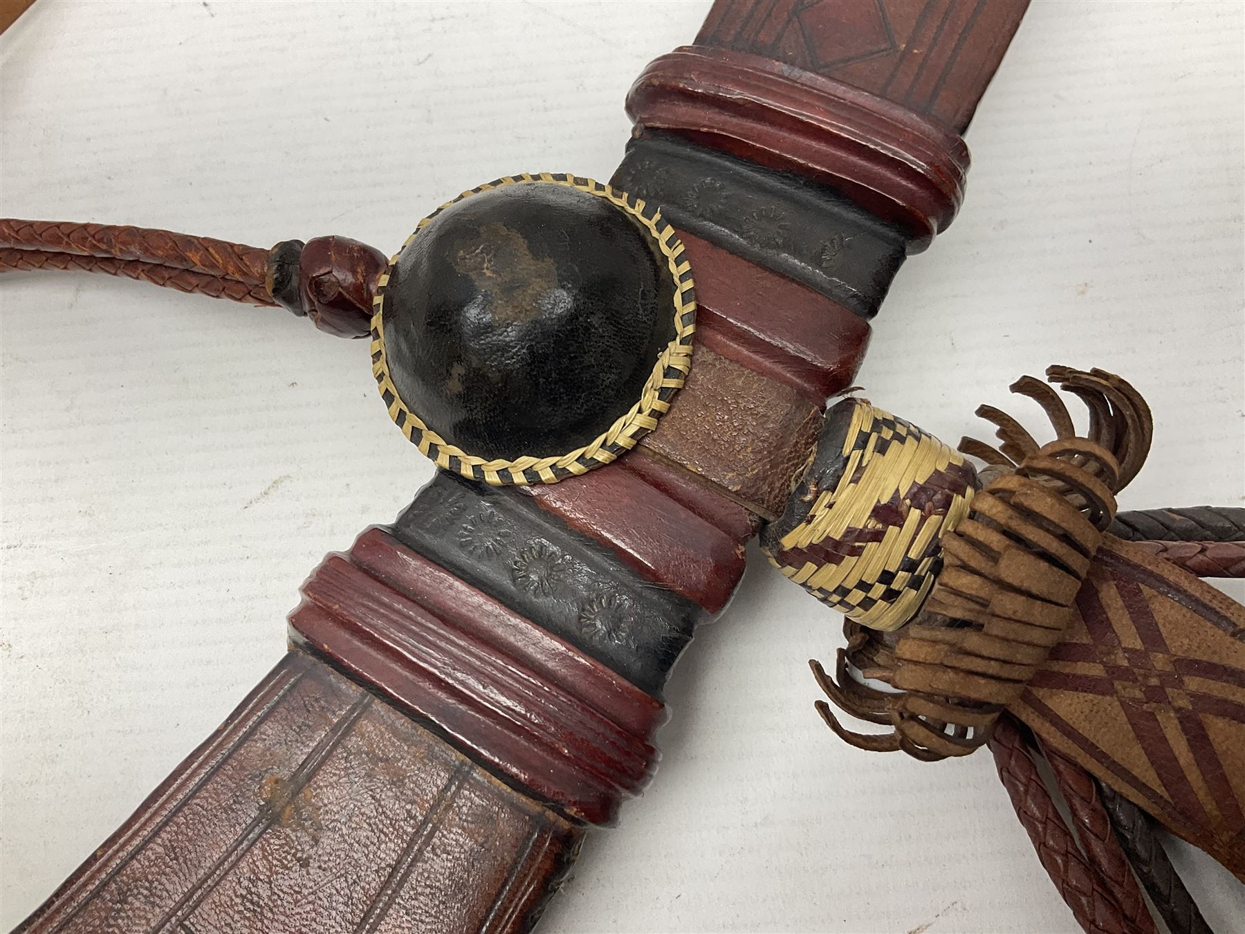 Mandingo sword with 63cm plain curving steel blade and leather covered grip with white metal ribbed spherical pommel; in decorative leather leaf scabbard with plaited tassels and shoulder strap L78cm overall