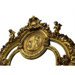 Large Italian Baroque design gilt wall mirror, the shell pediment over circular panel depicting classical female flute player with dancing putto within a tree landscape, the stepped arched upper frame surmounted by musical instrument playing putto and trailing flower heads, central bevelled mirror plate surrounded by plain segmented mirror plates, acanthus leaf moulded outer frame and foliate moulded inner slip