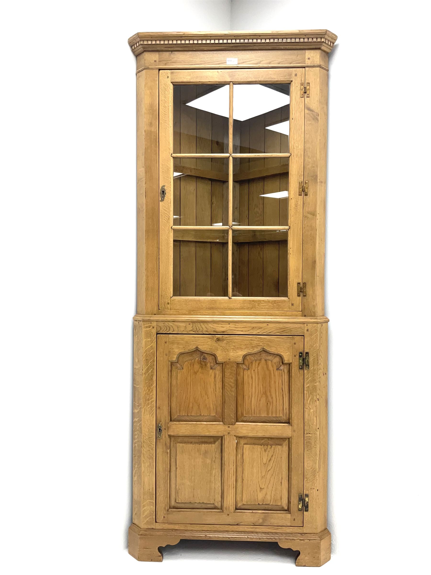 Oak corner cabinet, projecting cornice, dentil frieze, single glazed door enclosing two glass shelves above bottom unit, single fielded door enclosing fitted interior 
