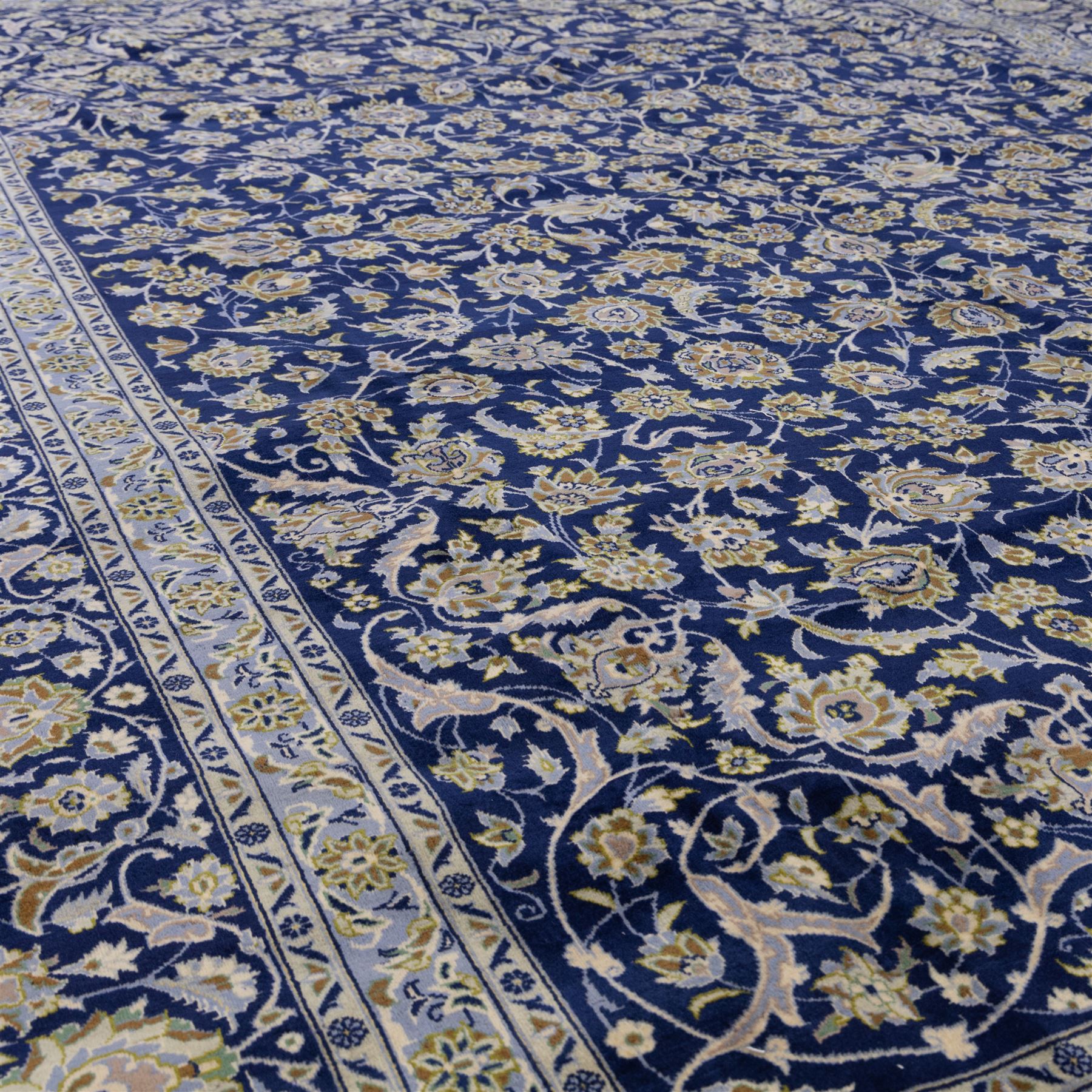 Central Persian Kashan hand-knotted rug, deep blue all-over field, finely decorated with dense scrolling floral sprays, palmettes, and flowering vines in ivory, soft gold, and pale green tones, enclosed by a multi-band floral border with corresponding guard stripes, with cotton fringe ends, signed Shah Abassi Workshop 