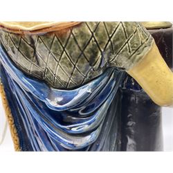 Composite table lamp modelled as a Roman Emperor donning blue robes, upon quatrefoil base modelled with rams heads and winged cherubs, H56cm excl fitting