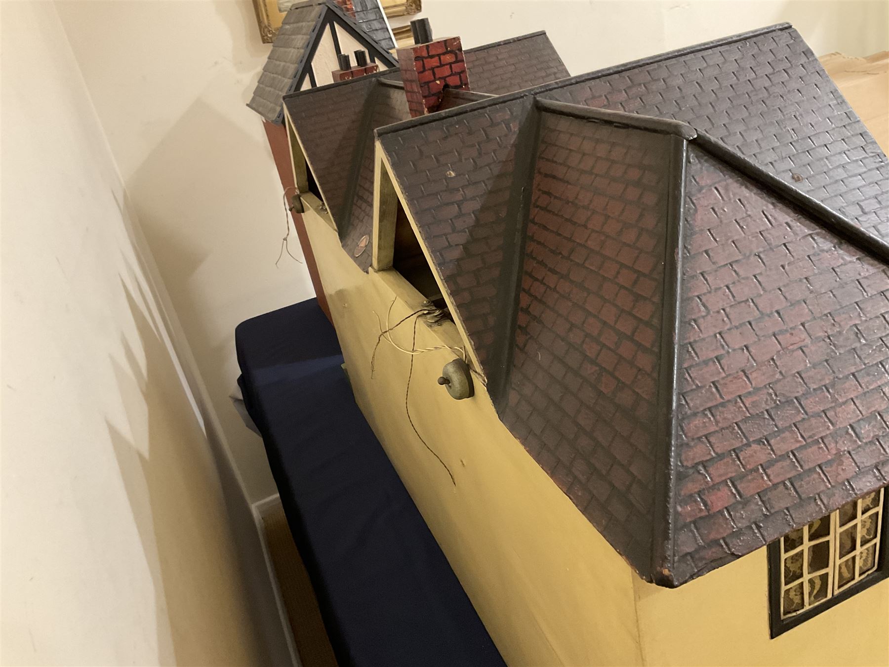 Large Tri-ang No.93 doll`s house in the 'Stockbroker's Range' c1935; two-storey double-fronted Tudor design, half timbered gables, two-storey bay windows, cream and mock shrubbery to front, opening metal framed windows with green shutters, red simulated tiled roof with chimney, integral garage with opening doors, front elevation has four hinged doors opening to reveal two bedrooms with fire places, living room, bathroom and kitchen with built in dresser and sink, entrance hall and staircase, side entrance with porch and seat and sun dial over on chimney stack; some wiring for electrical lighting; metal Tri-ang Toys disc verso; comprehensively furnished H66cm L117cm D43cm