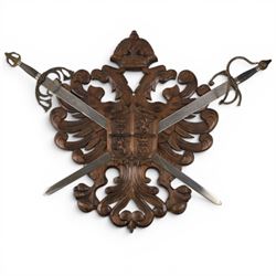 Carved wooden wall plaque, decorated with foliate scrolls, with two reproduction swords attached, together with five other wooden plaques with foliate scrolls and shields