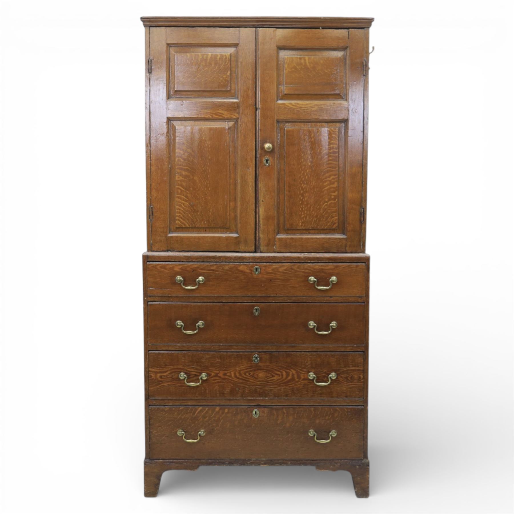 18th century oak press cupboard on chest, the moulded cornice above a pair of fielded panel doors enclosing shelved interior, the base fitted with four long graduated drawers with brass swan neck handles and shaped escutcheons, raised on bracket feet