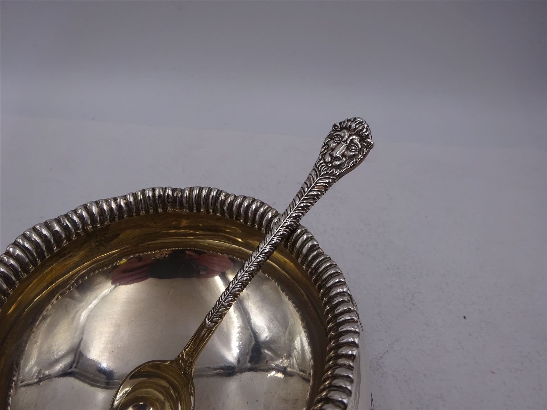 Early 20th century silver open sucrier, of circular form, with fluted gadrooned rim and decorated in relief with floral swags, united by three lion mask mounts and upon three paw feet, hallmarked Z Barraclough & Sons, London 1912, H6cm, D11cm, with similar spoon with lion mask finial, hallmarked London 1912, maker's mark indistinct