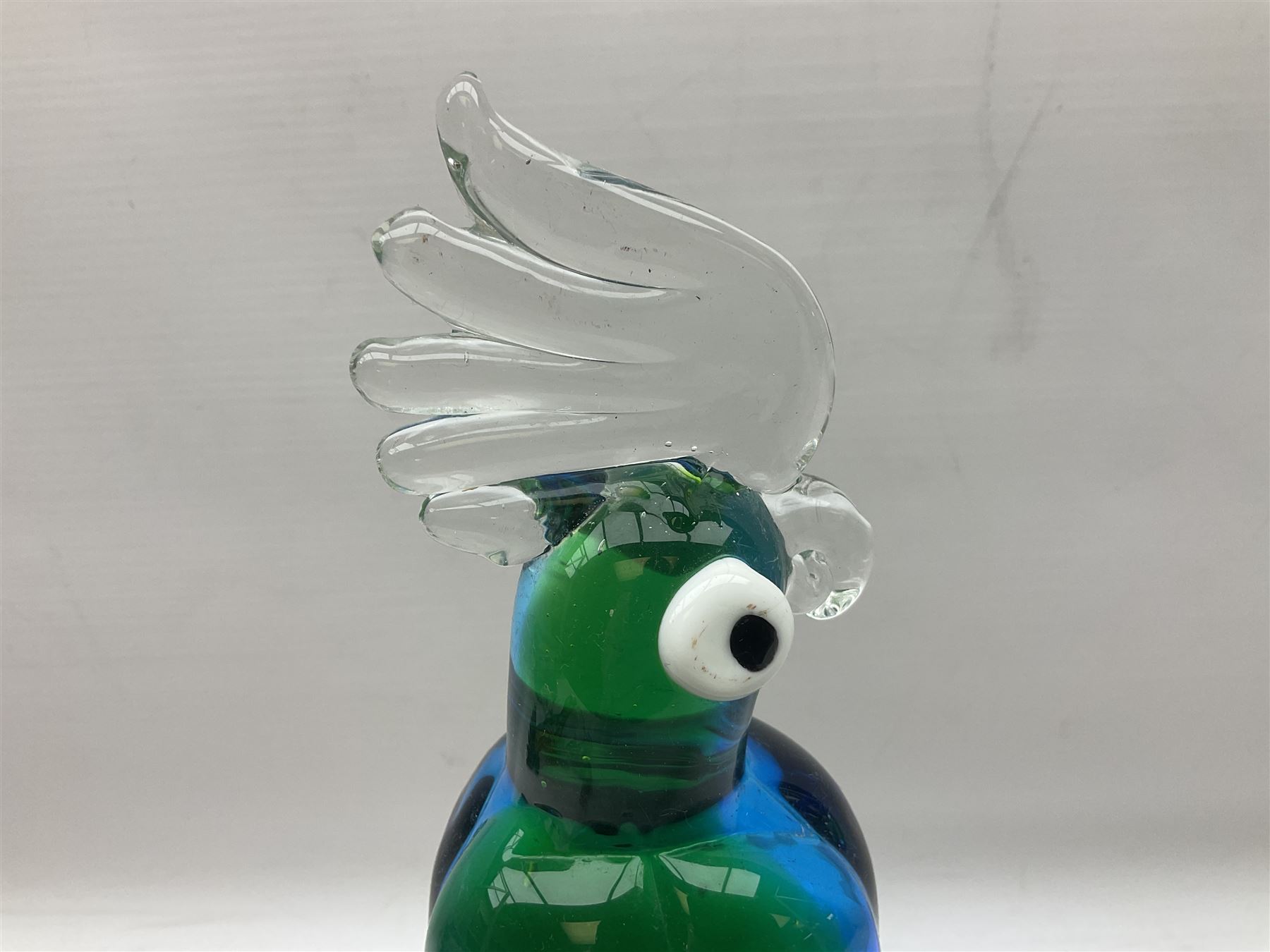 Three Murano style glass cockatoo parrots, the first with mottled yellow, red and orange body, clear outstretched wings, dark blue beak and red crest, raised upon clear stylised base, the second smaller parrot with merging blue and green body, and further with pink striped body, tallest H40cm