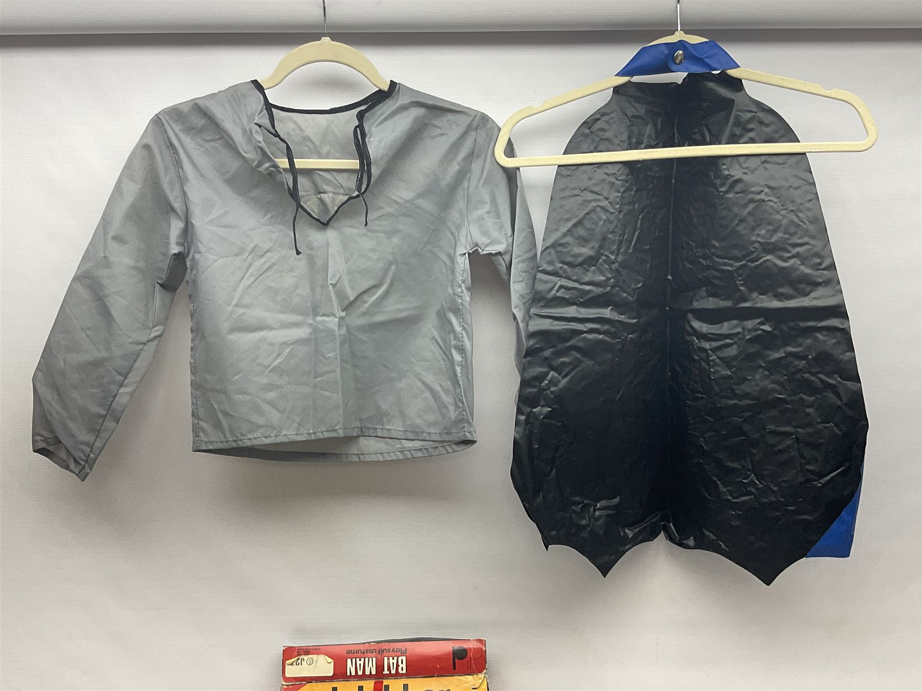 Two Boxed Batman Playsuit Costumes - 1960s 20th Century Original Play Suit, black eye mask, plastic vinyl cape/gauntlets, leather style belt, blue/yellow shirt, with Bat motif and blue/yellow pants; in original illustrated lidded box; and 1976 Decker Batman Playsuit costume, vinyl cape/ mask/gloves/boot tops/yellow belt, grey cloth top and pants; in original illustrated box (2)