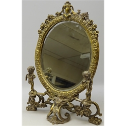  Cast brass toilet mirror with oval bevelled glass panel on open scrolling base, mounted with two putto, on paw feet, H56cm   