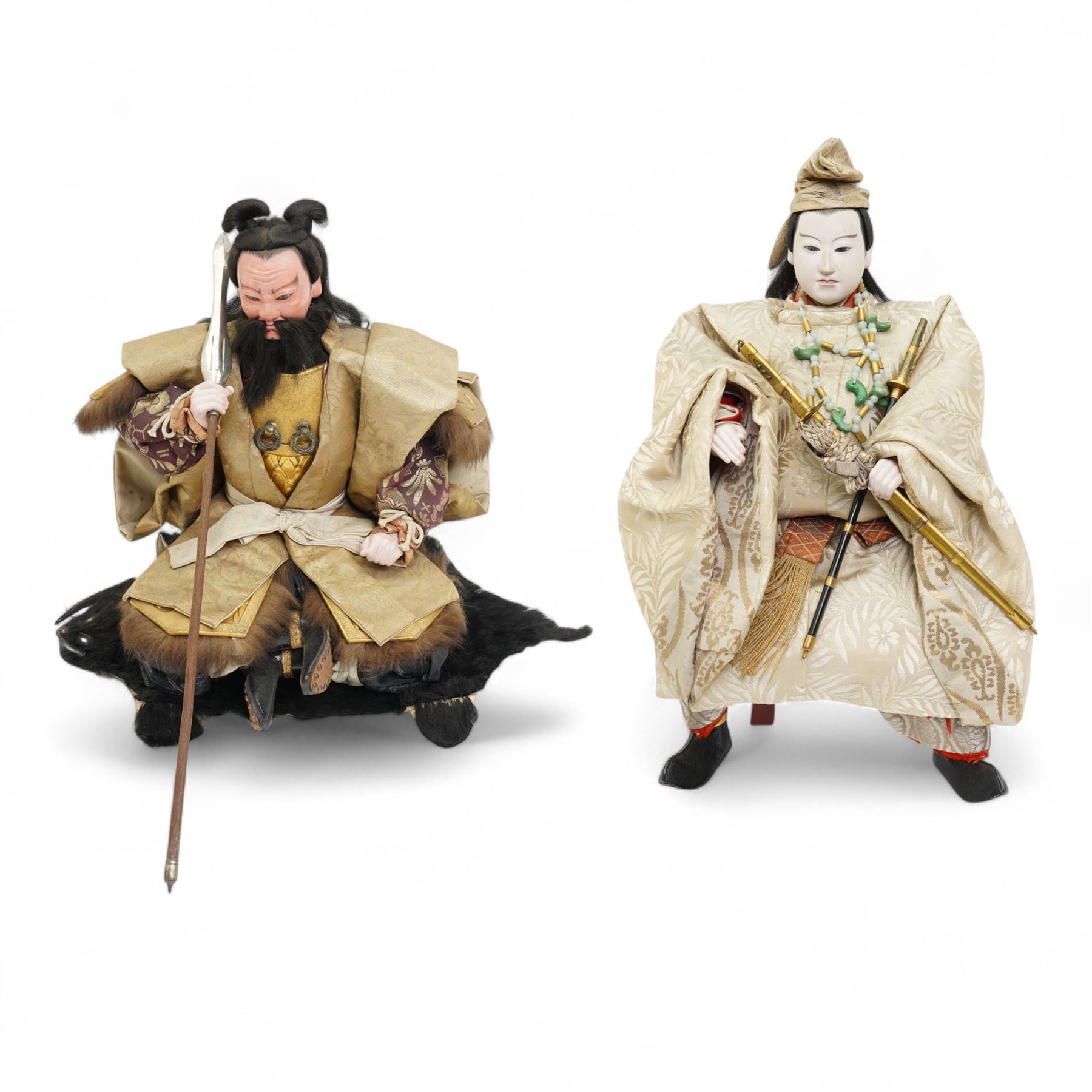 Two early 20th century Japanese 'Musha-ningyo' or Warrior Doll figures, costumed with distinctive armour and attributes, the first seated on lacquered red stool the other on a taxidermy rug, seated figure H44cm (2)