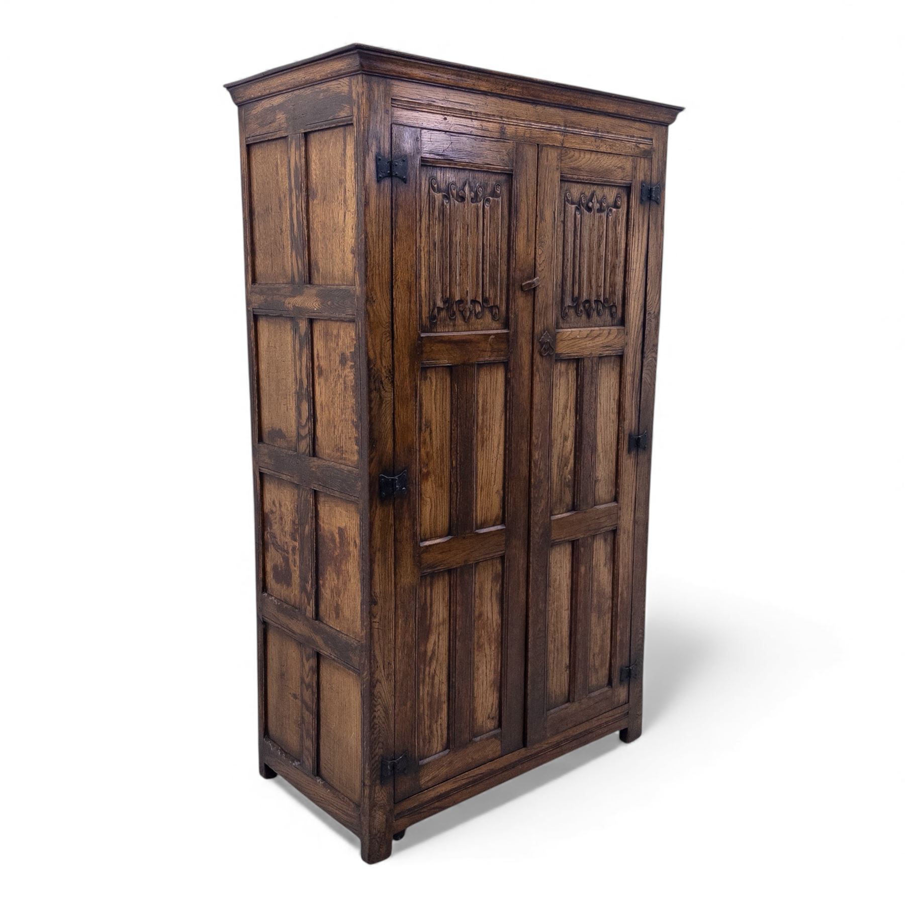 Mid 20th century oak double wardrobe, the rectangular top above twin panelled doors with carved linenfold decoration and wrought iron hinges, raised on block feet
