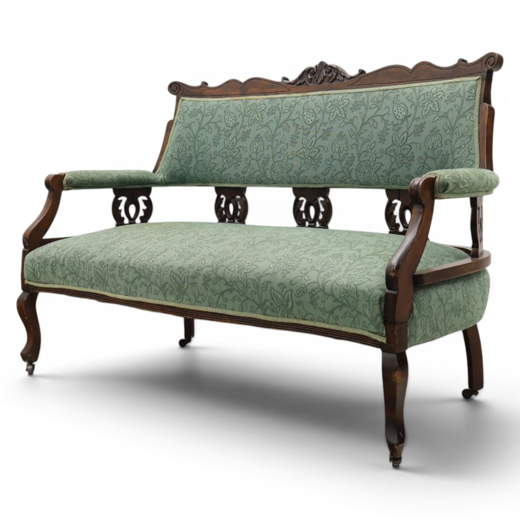 Edwardian mahogany framed sofa, shaped cresting rail with scroll terminals and carved foliate pediment, upholstered back and swept arms in green foliate fabric, pierced splat supports, serpentine front seat rail, on cabriole supports terminating in castors