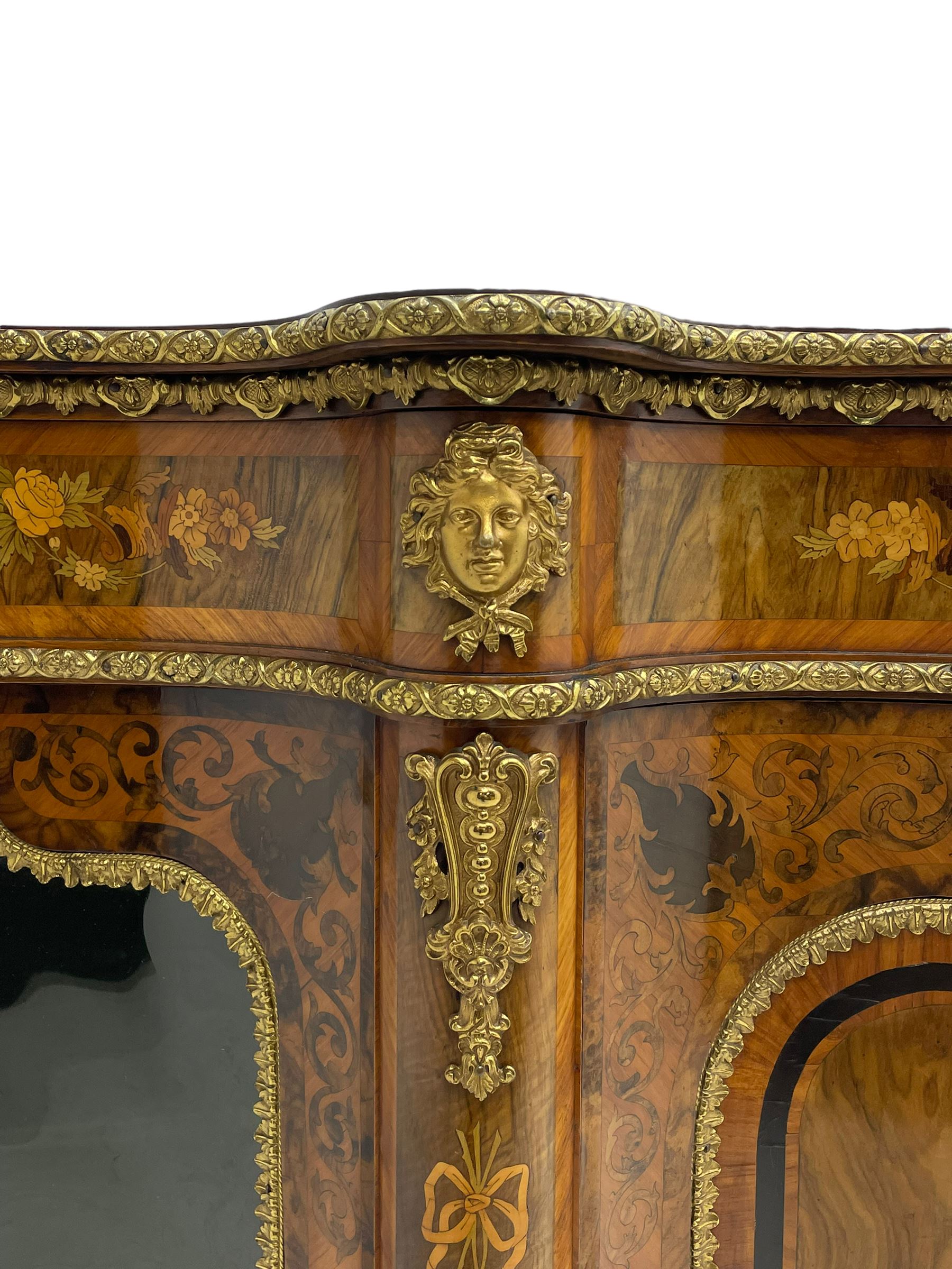Victorian design inlaid figured walnut credenza sideboard, shaped form with crossbanded and book-matched top, the frieze rails inlaid with foliage scrolls and flower heads, central panelled door inlaid with floral urn flanked by two glazed doors, on shaped plinth base inlaid with foliate decoration, mounted by cast gilt metal masks and floral egg and dart beading 