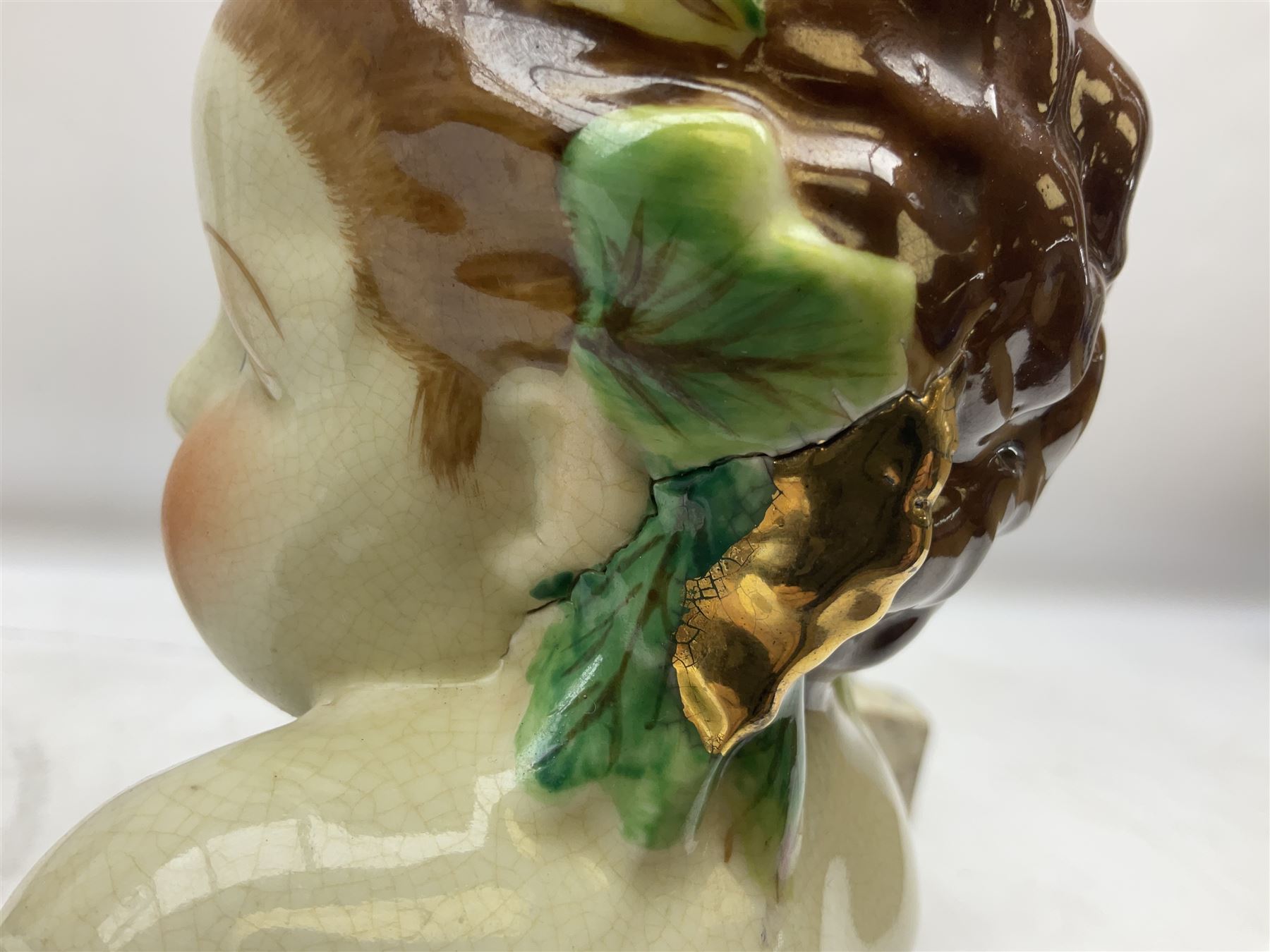 19th century pair of hand painted ceramic busts of children, together with a third similar example of a putti with a crown of ivy, tallest H23cm 