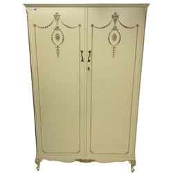 French classic design cream painted double wardrobe, the doors decorated with gilt and cream applied urn motifs with extending bell-flower festoons and ribbon twists, enclosing shelf and hanging rail, shaped apron on acanthus cabriole feet