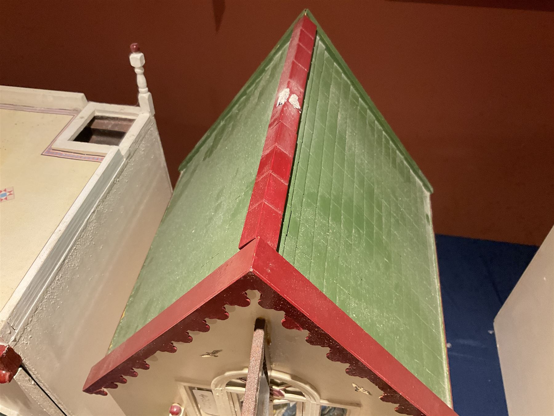 Seagull Pub - scratch-built wooden doll's house as a two-storey gable fronted public house painted in white green and maroon; the hinged front with ground floor veranda and window over opening to reveal two fully furnished rooms with dog-leg staircase and well stocked bar with bar-tender L31cm H62cm D37cm; together with Corner Shop and Dollies Pantry; a similarly painted scratch-built wooden two-storey flat-roofed doll's house as a well stocked ground floor grocery shop with stairs up to two further fully furnished rooms and more stairs giving access to a roof terrace L46cm H57cm D33cm (2)