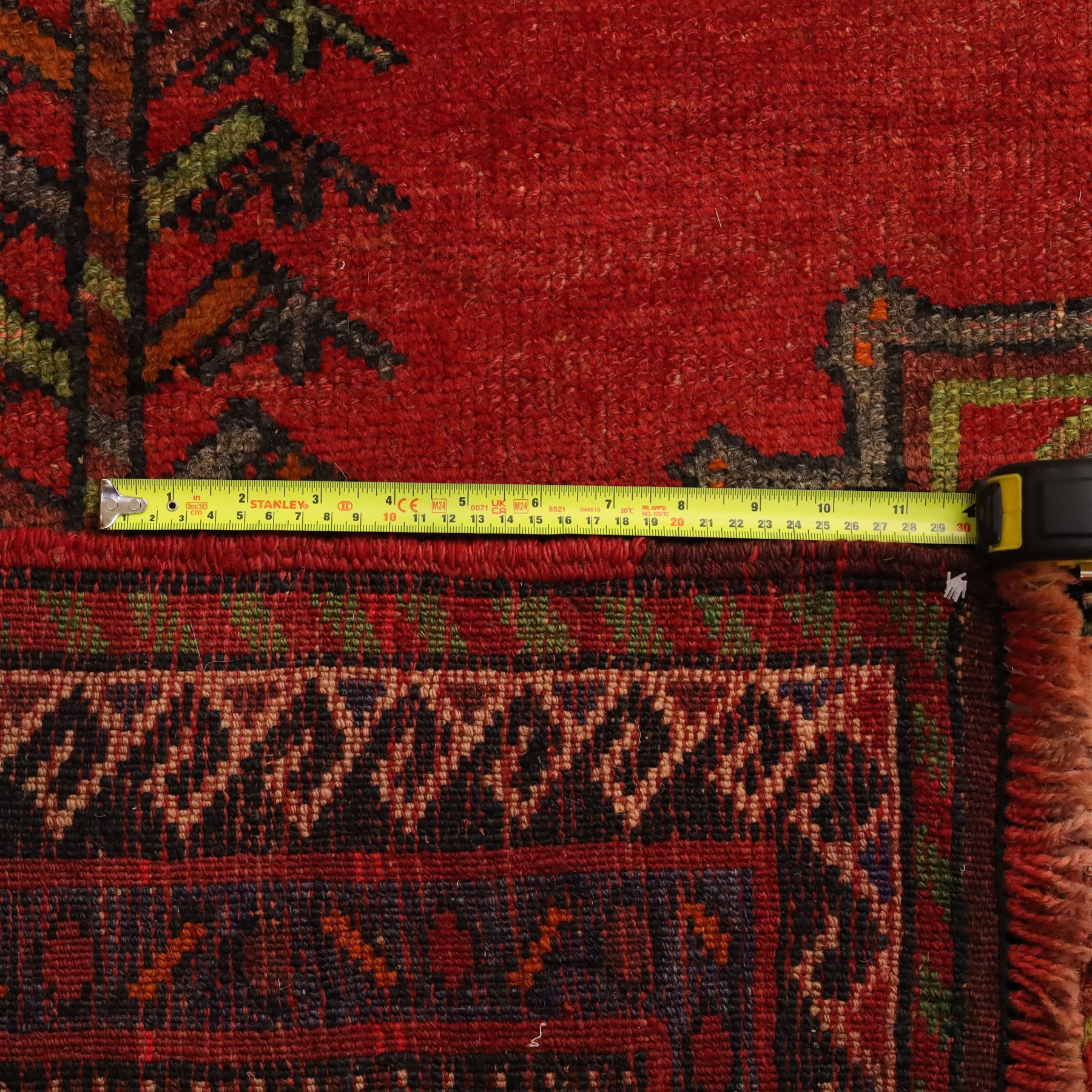 North East Persian Kurdish hand-knotted carpet, madder red field with three vertical and central stepped octagonal medallions enclosing angular geometric motifs with scattered tribal devices, framed by multiple narrow borders with latch-hook patterns, enclosing a bold main border of repeating geometric motifs, palette with indigo, dark brown and soft green tones, 