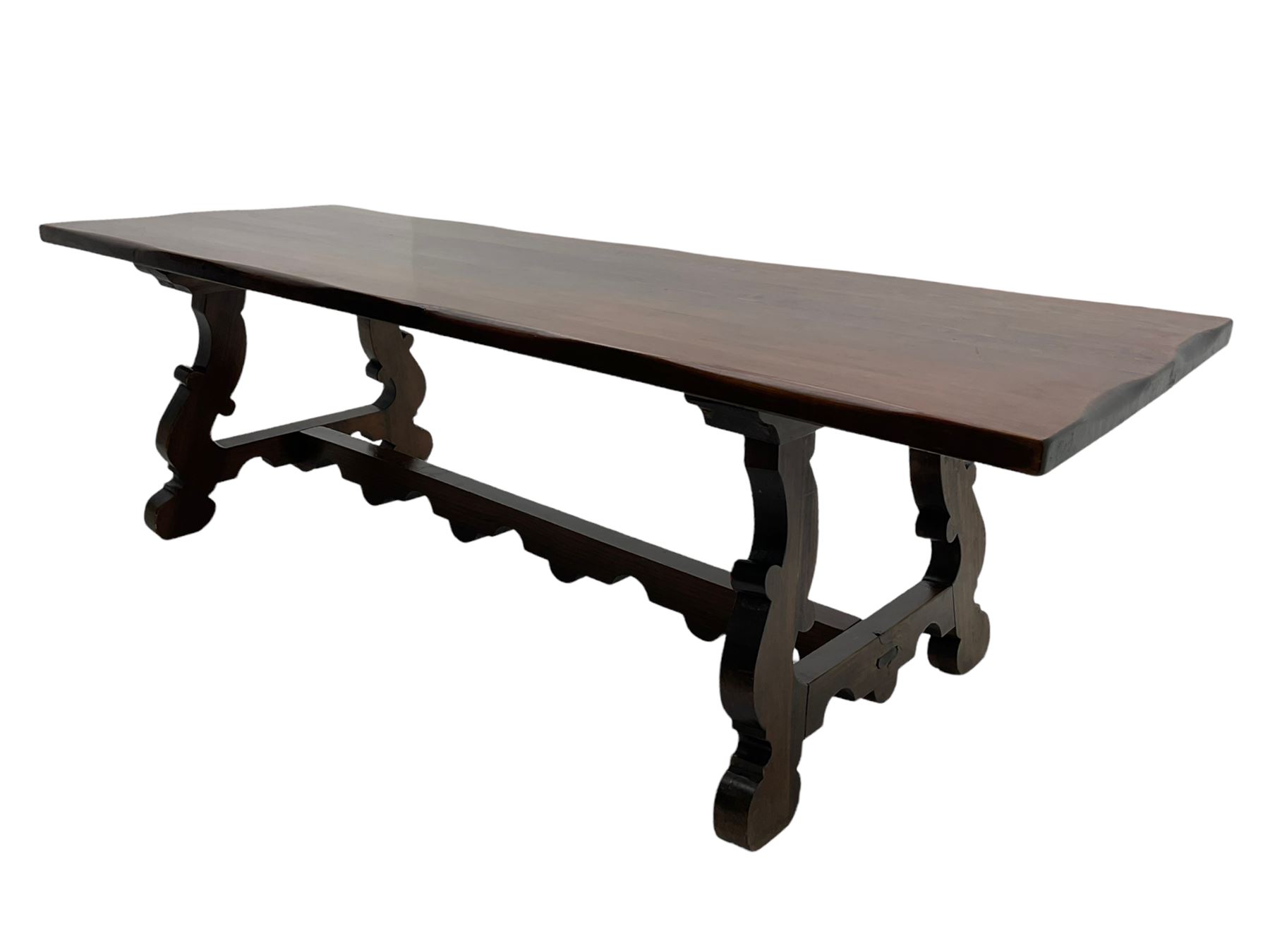 Large Spanish hardwood dining table, on shaped open ends supports joined by stretcher 
