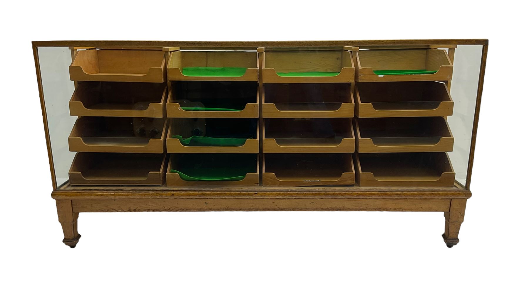 Early 20th century oak framed haberdashery shop counter, glass panel exterior enclosing sixteen graduating drawers with oak fronts and handles, raised on shaped tapering supports 