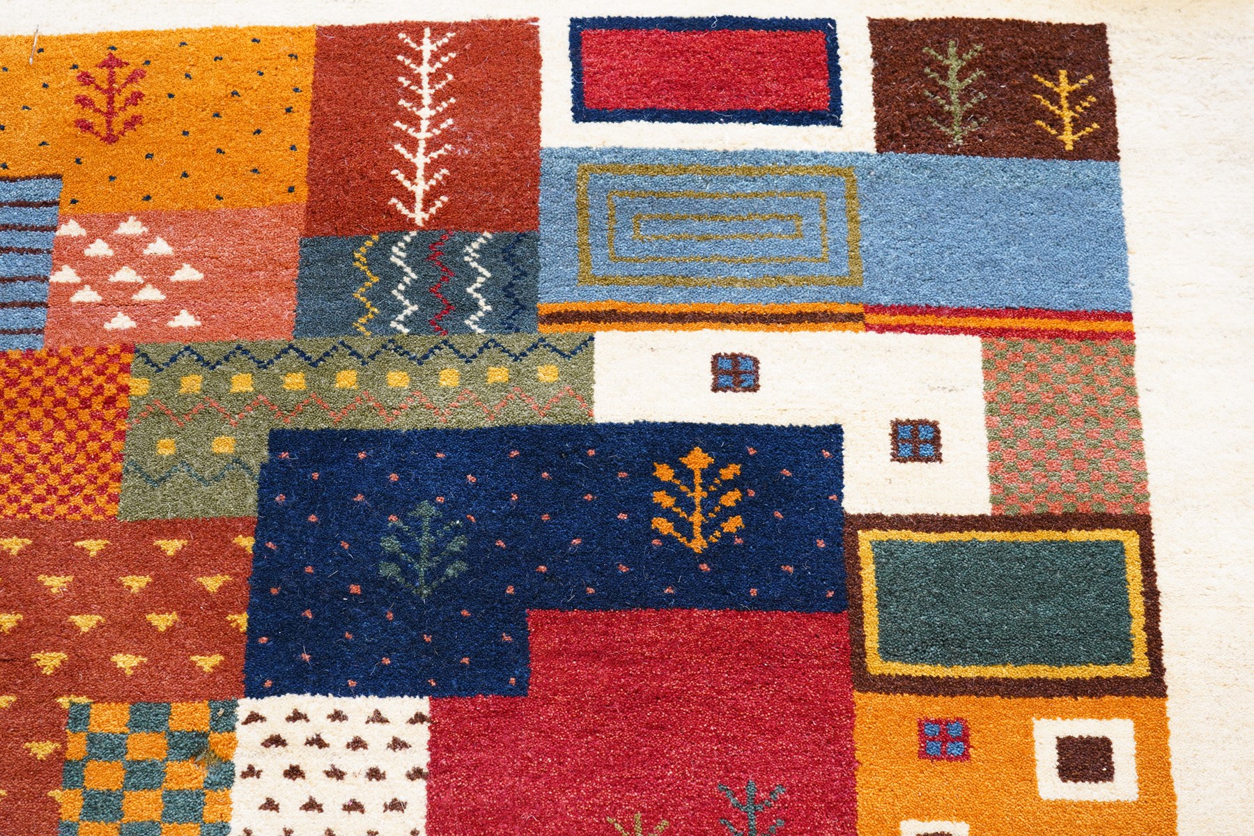 Persian style Gabbeh Loribaft design ivory ground rug, the vibrant field decorated with geometric patchwork design panels with interspersed stylised tree motifs, enclosed by a wide ivory guard band