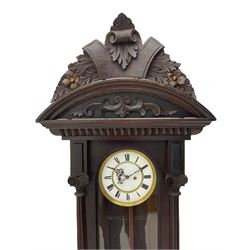 A late 19th century German Vienna style weight driven wall clock c1880, with a predominant arched pediment and applied carving, case with glass side panels (one missing) and a glazed full-length arched door flanked by reeded columns with decorative capitals, 7' two-piece white enamel dial with roman numerals, minute markers and pierced steel gothic hands, pendulum with a wooden rod, pressed brass bob and beat plate, eight-day weight driven movement striking the hours and half hours on a coiled gong. With brass cased weights.



