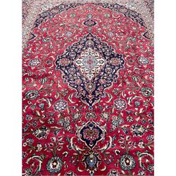 Central Persian Kashan crimson ground carpet, central  floral pole medallion with matching spandrels within a field of scrolling palmette motifs and foliage, the heavily banded indigo border with repeating plant motifs interlaced with scrolled branches