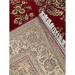 Persian design crimson ground carpet, central rosette medallion surrounded by clusters of flower head motifs, scrolling floral design spandrels, the border decorated with repeating stylised plant motifs within guard stripes 