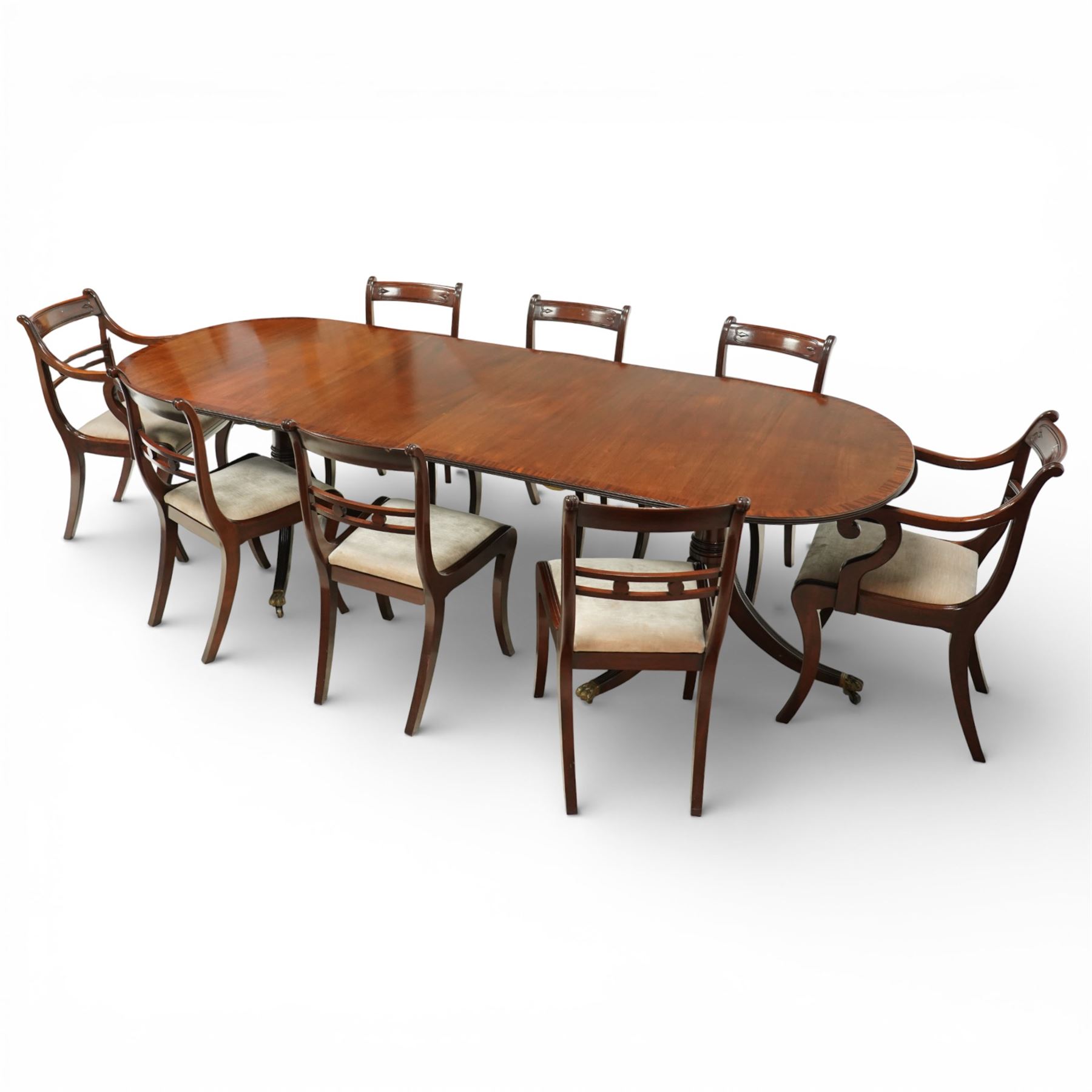 Arthur Brett & Sons - Regency design mahogany extending dining table and eight chairs, the oval top with rounded ends and two extension leaves, raised on twin pedestal supports with swept legs terminating in brass caps and castors, accompanied by a set of eight chairs comprising six single chairs and a pair of carvers, the chairs with curved backs and horizontal splat rails, upholstered seats, sabre legs and scrolling arms to the carvers
(Extends to 252cm)
(Chairs H 86cm, W 52cm)